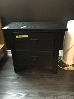 Front view of black wood nightstand showing two drawers and metal pulls.