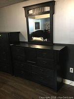 Full view of black wood dresser with mirror on a grey wall and brown floor, showing the design and size proportions.