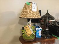 Lion King Child's lamp with animal print shade and cartoon lion base next to a box of light bulbs and two other lamps