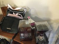 Four assorted ladies purses of various styles and colors on wooden chair and surface, including black leather purse, light pink purse, black and white handbag, and brown purse partially visible. Also visible are boxed makeup brush sets and a packaged drinking game.