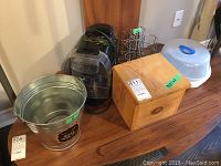 View of the entire lot including Tassimo coffee maker, metal pail, wooden box, coffee pod caddy, and baby bottle container.