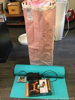 Photo showing pink fabric hamper with detachable liner, teal rolled yoga mat, Garmin GPS device with cables, pair of dumbbells, Skateez skate trainers box