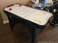 Front angle view of air hockey table showing playing surface, four red strikers and one red puck with black frame and legs.