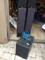 Two Paradigm floorstanding speakers stacked behind subwoofer on patio with cables visible