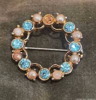 Front view showing alternating blue stones and faux pearls in gold-tone circular setting, missing one stone