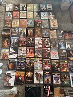Wide shot showing bulk of DVD cases laid out grid-style on carpet; mix of used and some sealed titles