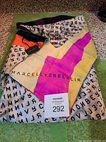 Folded Marcell Von Berlin silk scarf showing logo print, color-block design and attached retail tag