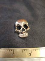 Front view of gold-tone skull brooch with rhinestone teeth beside ruler