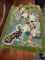 Full view of needlepoint wall hanging showing bird, floral design, velvet border and hanging tabs
