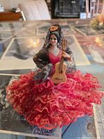 Front view of seated flamenco dancer doll in red lace dress holding guitar