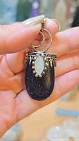 Front view of pendant showing blue goldstone cabochon and marquise opalite moonstone, ornate silver-tone bezel and bail