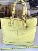 Front view of yellow Coach Ashley tote showing logo, handles and ruler for scale