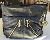 Front view showing pebbled leather, dual diagonal zip pockets, MK charm