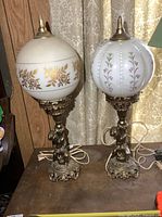 Full view of both brass table lamps with mismatched painted milk glass globes
