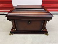 Front view of mahogany veneer jewelry chest showing keyhole, column trim and brass feet