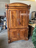 Front view of closed cherry veneer armoire showing four paneled doors and arched crown