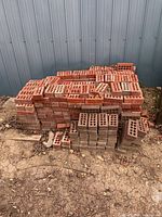 Stack of perforated red and brown clay bricks against metal siding