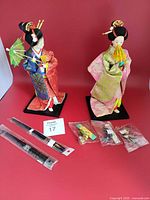 Two Geisha dolls, packaged sword accessories, small bagged trinkets overview