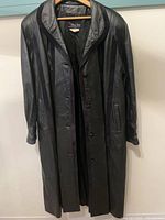 Front view of black leather full-length coat on hanger showing button closure and pockets