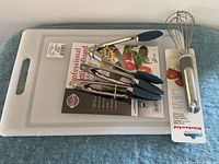 Whisk, three tongs and cutting board overall view