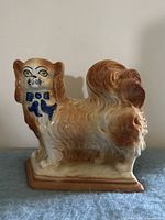 Front view of ceramic Pekingese figurine showing blue bow and coloration