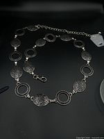 Full view of silver-tone metal concho belt laid flat showing alternating link design and lobster clasp