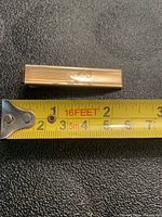 Front view of gold filled tie clip beside tape measure showing 2 in length