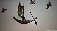 assembled sculpture on wall: wood boat, brass sail, three birds