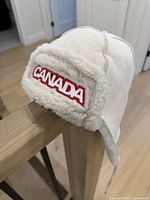 Front view showing cream hat with red Canada wordmark and faux shearling lining