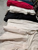 Row of folded garments showing color variety fuchsia, teal, white knit, black, ivory