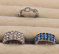 Three rings displayed on ring slots: top fixed band with clear stones, bottom two stretch bands with clear and blue stones