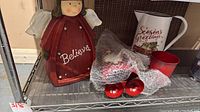 Red ceramic angel, white metal pitcher, bubble-wrapped metal Santa on shelf