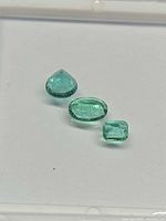 Close view of three loose emeralds showing shapes and colour