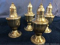 Four antique sterling silver shakers on black cloth background. View shows urn-shape and decorative beaded trims.