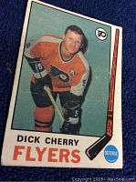 Front view of 1969-70 O-Pee-Chee Dick Cherry rookie hockey card in Philadelphia Flyers orange jersey, holding hockey stick.