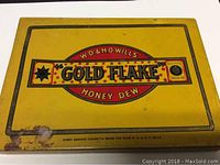 Top side of yellow flat rectangular tin with red and black W.D. & H.O. Wills Gold Flake Honey Dew logo, some rust and wear visible