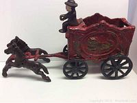 Side view of entire cast iron toy wagon with two horses and driver figurine. Shows overall structure, colors, and details.