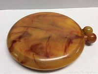 Top view of round Bakelite compact with butterscotch and marbled reddish-brown patterns, showing glossy surface.