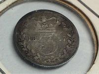 Close up of the reverse side of the 1877 silver 3 pence coin showing crown, denomination, wreath and date.