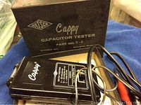 Capacitor tester handheld device with Watsco branding and model number on the box in background.