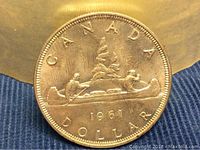 Obverse side of 1961 Canadian silver dollar showing two men paddling a canoe with goods.