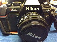 Front view of Nikon N2020 camera with lens cap on the lens, showing Nikon logo and N2020/AF markings.