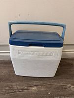 Full view of blue-lid white Coleman cooler with handle raised