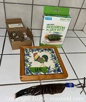All four items laid out: boxed microgreens kit, bird nest ornament in open box, rooster tile trivet, beaded feather