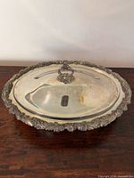 Overall view of ornate silver-plated covered dish with lid on wooden surface