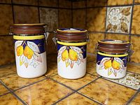 Three ceramic canisters of varying sizes with lemon motif and clamp lids