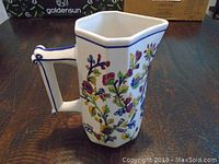 Front side view of the hexagonal ceramic jug showing colorful floral designs and handle with blue trim.