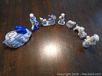 Photo showing all 7 ceramic pieces arranged in a row on a wooden surface, including the bunny shaped box and various figurines of children and animals.