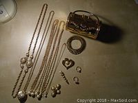 Gold tone jewelry collection laid out including four chain necklaces with pearl accents, a wide cuff bracelet, heart pendant, spiral drop earrings, small hoop earrings, and clip-on pearl cluster earrings.