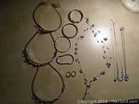 Overview of assorted silver tone jewelry on a surface, showing necklaces, bracelets, bangles and earrings